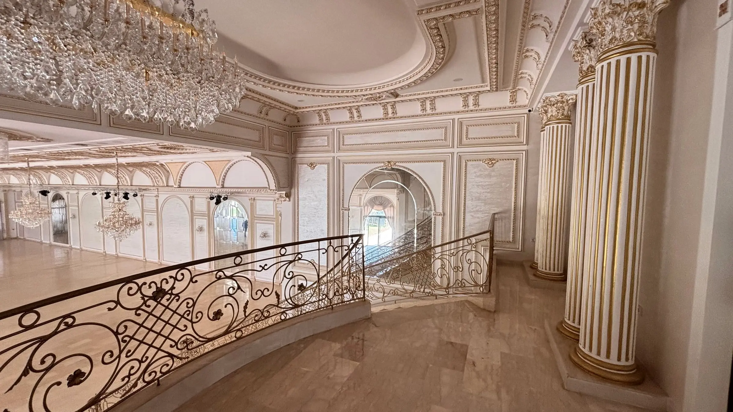 Escalier courbe à rampe en fer forgé, colonnes et marbre, salle vide