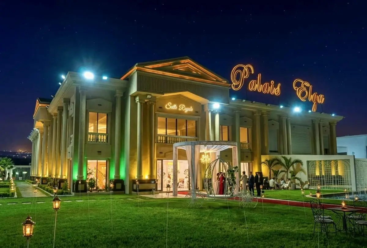 Façade éclairée de vert et d’or la nuit, enseigne allumée, pelouse