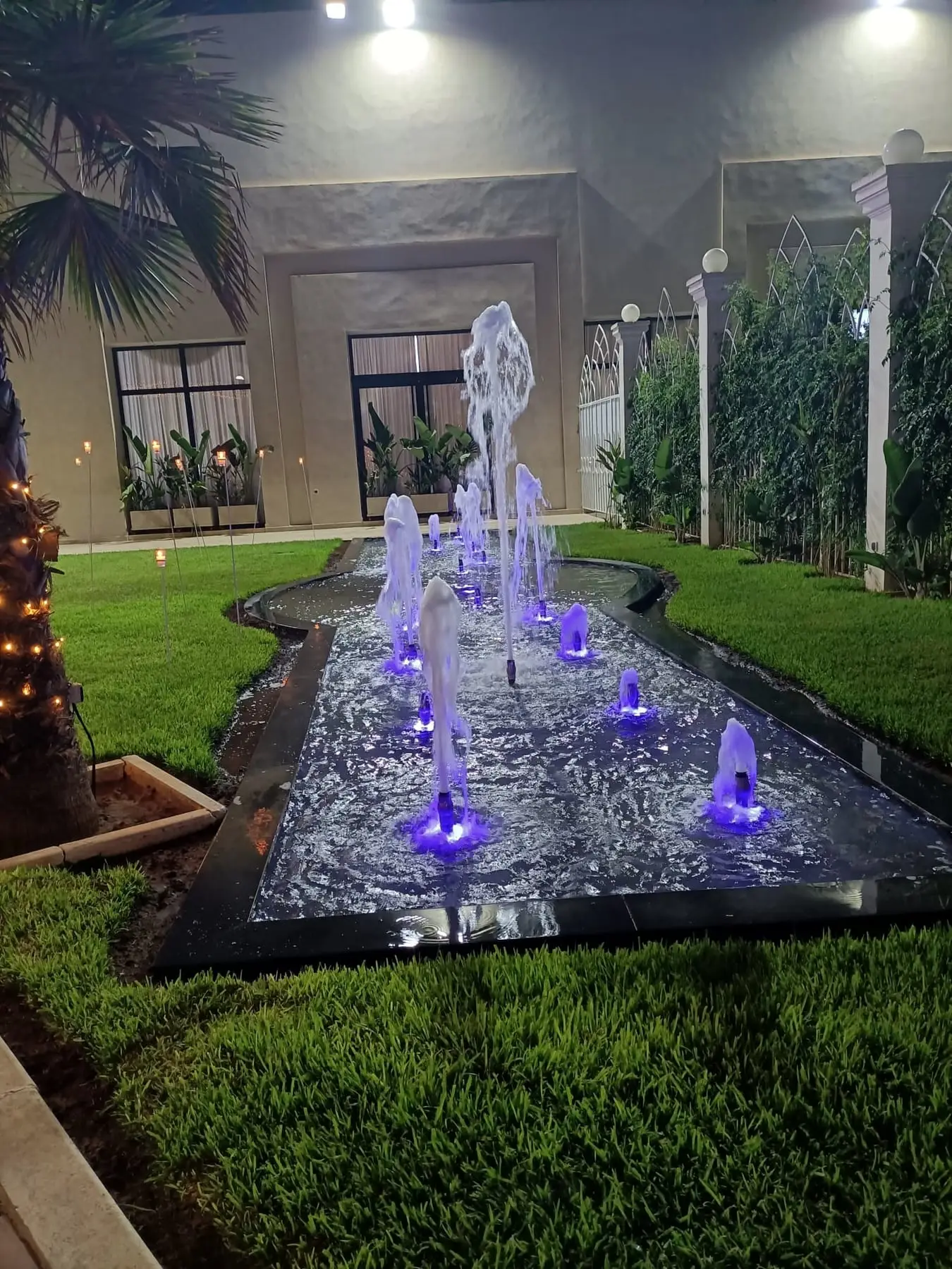 Fontaines illuminées de violet au pied des colonnes, la nuit