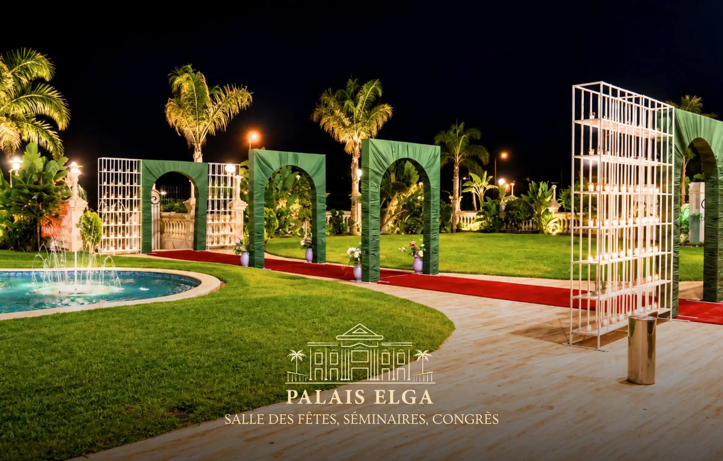 Jardin la nuit : piscine illuminée, palmiers, arches fleuries vertes sur tapis rouge