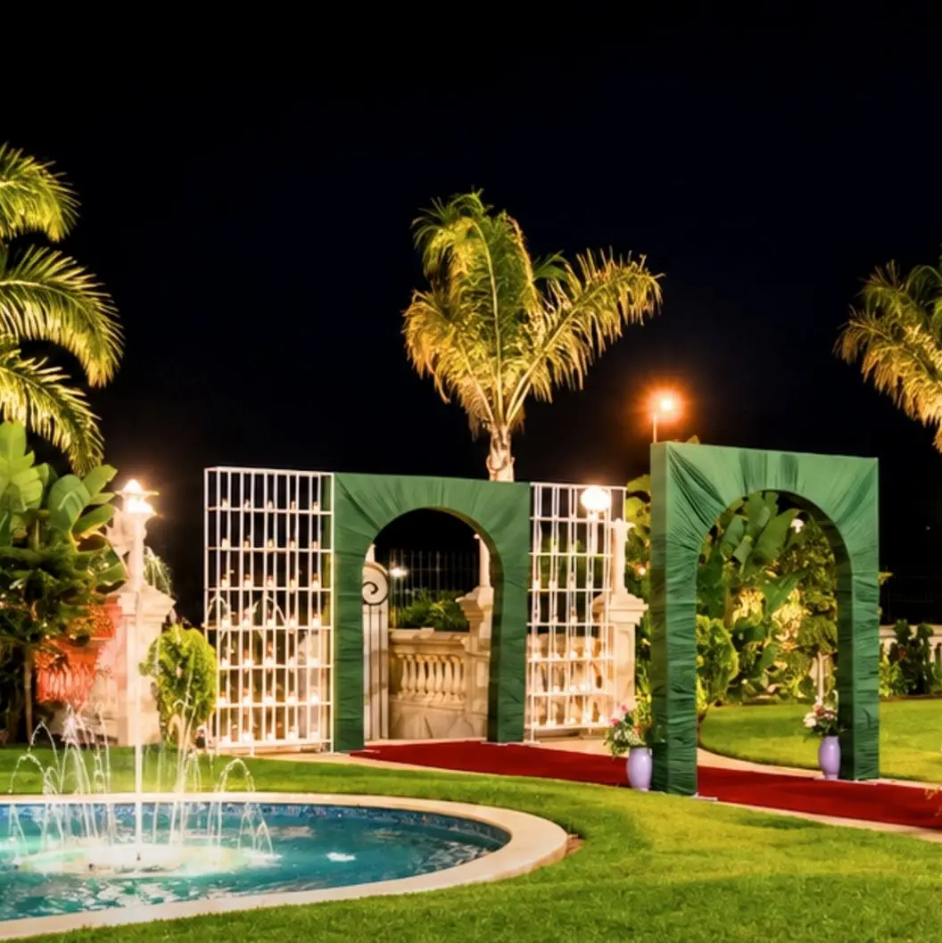 Le jardin la nuit : bassin illuminé, palmiers, arches vertes sur le tapis rouge