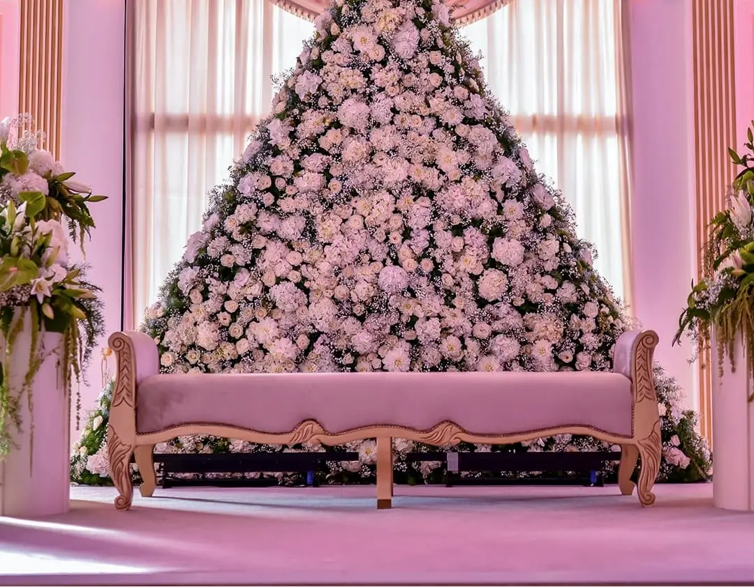 Pink kosha: settee in front of a wall of white flowers under an arched window