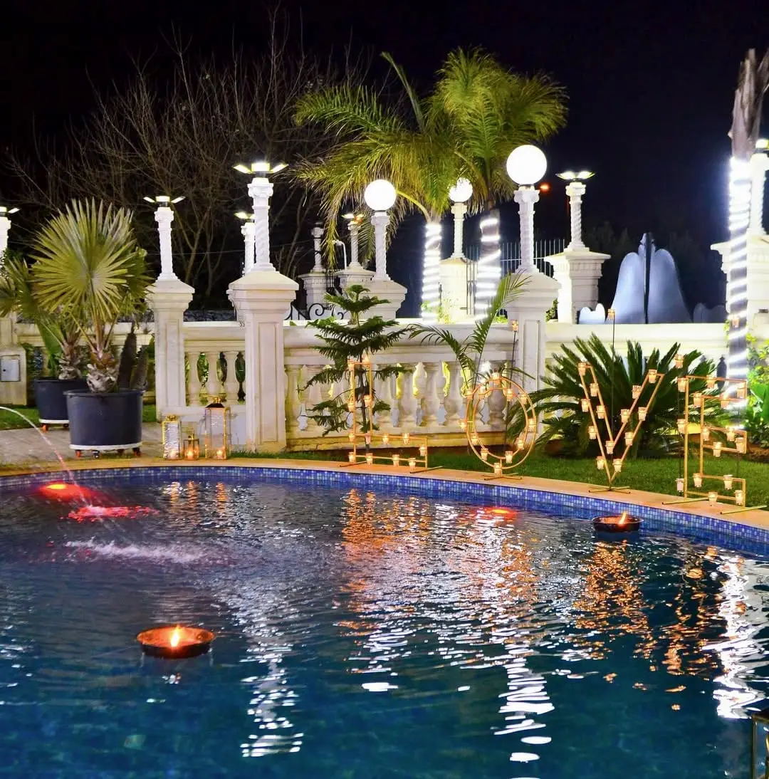 Piscine la nuit, bougies flottantes et vasques de feu, palmiers et balustrade