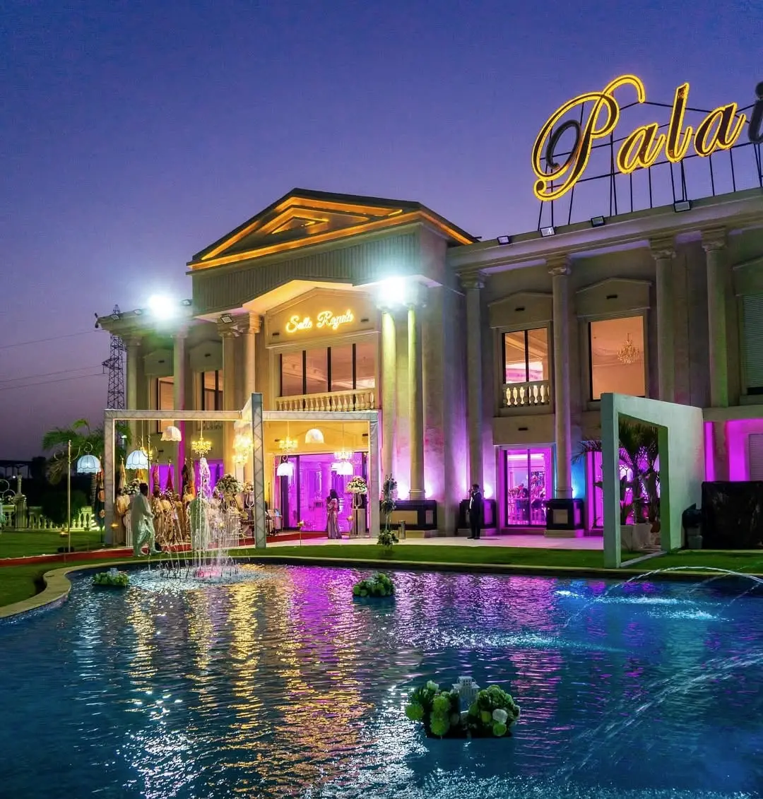 The violet-lit façade reflected in the pool at night